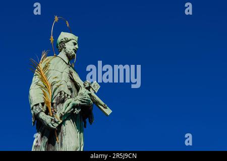 Heiliger Johannes von Nepomuk, Schutzpatron und Märtyrer von Böhmen. Bronzestatue mit Kruzifix, errichtet auf der Prager Karlsbrücke im Jahr 1683 (mit blauem Himmel und Kopierspieß Stockfoto