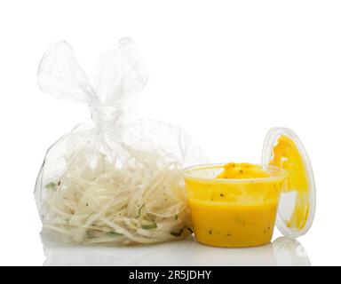 Bei einem indischen Essen zum Mitnehmen wurden Sachen hinzugefügt (aber nicht immer gegessen). Gehackte Zwiebeln in einer Plastiktüte und gelbe Dippsoße. Stockfoto