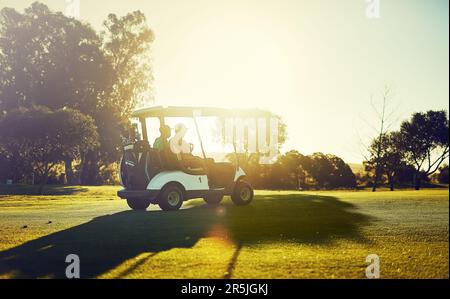 Sich in den Schwung zu bringen. Zwei Golfer, die in einem Wagen auf einem Golfplatz reiten. Stockfoto