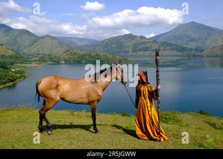 eine indonesierin trägt moderne Ulos (traditionelles Batakneskleid), während sie Pferde hütet, auf der Seite des Tobasees Stockfoto