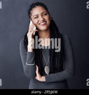 Mobiltelefone sind definitiv ein grundlegendes Bedürfnis. Studiofoto einer jungen Frau, die mit ihrem Handy vor grauem Hintergrund spricht. Stockfoto