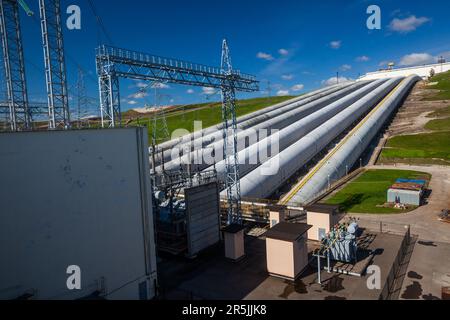 Wasserkraftwerksrohre und elektrische Türme und Transformatoren gegen blauen Himmel Stockfoto