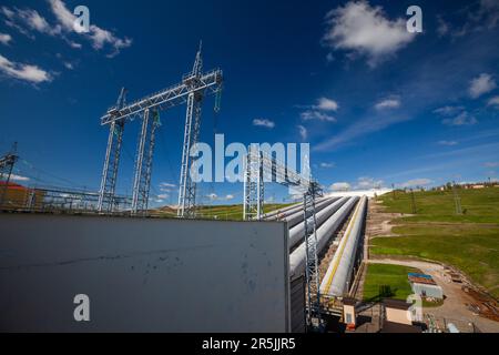 Sergijew Posad, Russien - 18. Mai 2022: Zagorskaja Wasserkraftwerk Rohre (rechts) und elektrische Türme am blauen Himmel mit Wolkenhintergrund Stockfoto