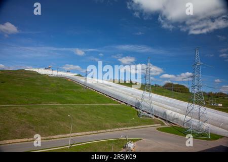 Wasserkraftwerksleitungen und Elektromasten auf Hügeln gegen blauen Himmel und Wolken Stockfoto