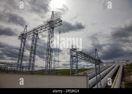 Elektrische Türme von Unterstationen und Wasserrohren auf grauem, wolkigen Himmelshintergrund Stockfoto