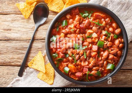 Mexikanische Charrobohnen mit Pintobohnen, Speck, Schinken, Chorizo, Chili-Paprika, Tomaten und Gewürze auf der Schüssel auf dem Tisch. Horizontal oben V Stockfoto