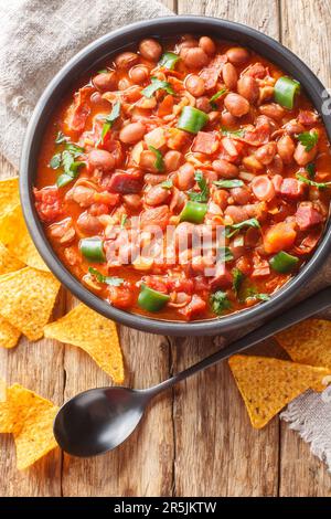 Mexikanische Charrobohnen oder Frijoles Charros mit Speck, Tomaten, Zwiebeln, Schinken und Jalapenos, die auf der Schüssel auf dem Tisch zusammengeschlossen sind. Vertikale Draufsicht von oben Stockfoto