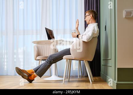 Ein positiver Mann mittleren Alters führt Videoanrufe auf einem Laptop Stockfoto