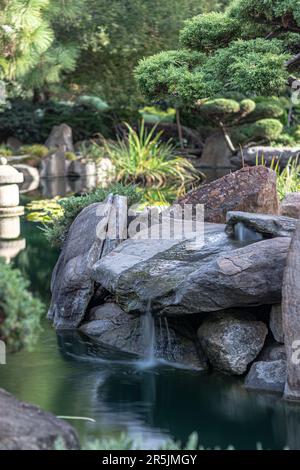 Üppiger japanischer Garten mit einem ruhigen Fluss und großen Felsen Stockfoto