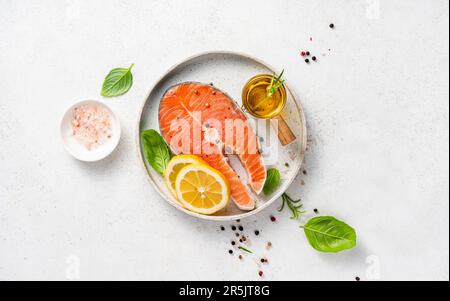 Frische rohe Lachssteaks mit Gewürzen, Zitronen und rosa Salz auf weißem Teller. Draufsicht auf Fische auf weißem Hintergrund. Keto-Rezept. Stockfoto