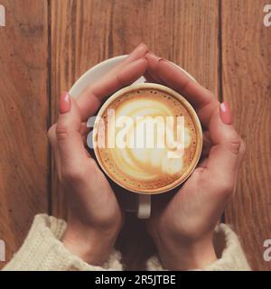 Weibliche Frauenhände mit Kaffeetasse mit Schaum und Herzmuster Stockfoto