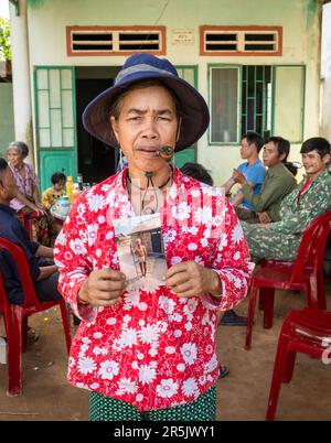 Eine Frau mittleren Alters aus der ethnischen Minderheit Kontum Province, Vietnam, raucht eine Pfeife und hält ein Foto von ihrem Vater, der ein Koteletttuch und einen Urlaub trägt Stockfoto