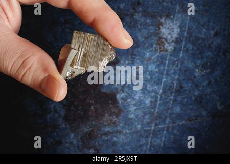 Ein weißer Mann, der ein Pyrit-Mineral in den Fingern hält, auf einem rostigen Metallhintergrund. Pyrit ist ein natürlicher Kristall, der durch die Sedimentation von entsteht Stockfoto