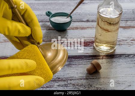 Ein Mädchen mit gelben Handschuhen reinigt einen Messingkerzenhalter mit Essig, Salz und einem gelben Schwamm Stockfoto