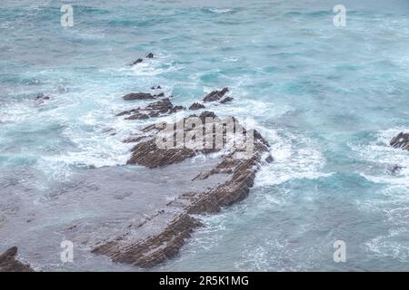 Felsige Klippen mit futuristischen Mustern an der Atlantikküste in der Nähe der Stadt Aljezur im Südwesten Portugals. Das Rauschen des Ozeans bei Sonnenuntergang. Stockfoto