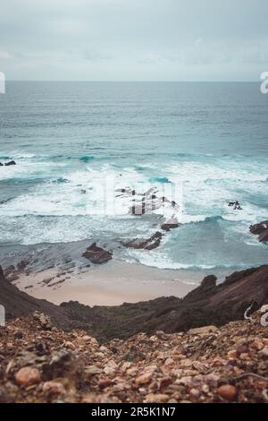 Felsige Klippen mit futuristischen Mustern an der Atlantikküste in der Nähe der Stadt Aljezur im Südwesten Portugals. Das Rauschen des Ozeans bei Sonnenuntergang. Stockfoto