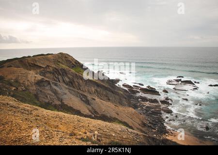 Felsige Klippen mit futuristischen Mustern an der Atlantikküste in der Nähe der Stadt Aljezur im Südwesten Portugals. Das Rauschen des Ozeans bei Sonnenuntergang. Stockfoto