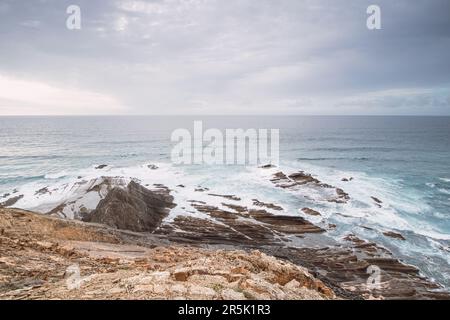 Felsige Klippen mit futuristischen Mustern an der Atlantikküste in der Nähe der Stadt Aljezur im Südwesten Portugals. Das Rauschen des Ozeans bei Sonnenuntergang. Stockfoto