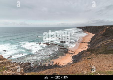 Felsige Klippen mit futuristischen Mustern an der Atlantikküste in der Nähe der Stadt Aljezur im Südwesten Portugals. Das Rauschen des Ozeans bei Sonnenuntergang. Stockfoto