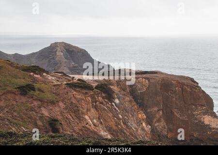 Ein abenteuerlustiger Mann, der am Rand einer Klippe steht, genießt den Blick auf die Atlantikküste in der Region Odemira im Südwesten Portugals. Ich wanderte im Ro herum Stockfoto