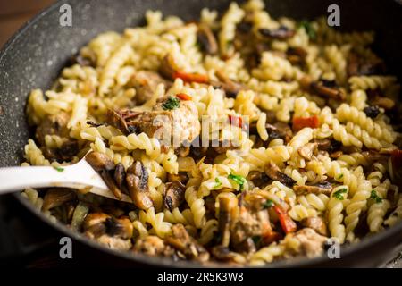 Vermicelli mit Pilzen, Fleisch und Gemüse in einer Bratpfanne auf einem Holztisch gekocht Stockfoto