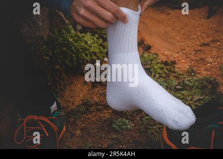 Ein junger Reisender, der auf seiner Pilgerreise am Fisherman Trail unterwegs ist, flickt seine Knöchelblasen und zieht eine neue Socke an. Die Härten langer Reisen. Stockfoto