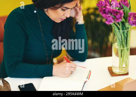Eine schöne Frau mittleren Alters, die sich Notizen in Notizbüchern macht Stockfoto