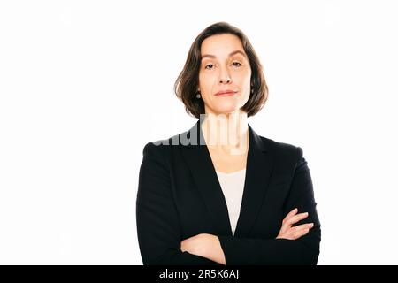 Studioporträt einer 45- bis 50-jährigen Frau, die auf weißem Hintergrund posiert und eine schwarze Jacke trägt Stockfoto