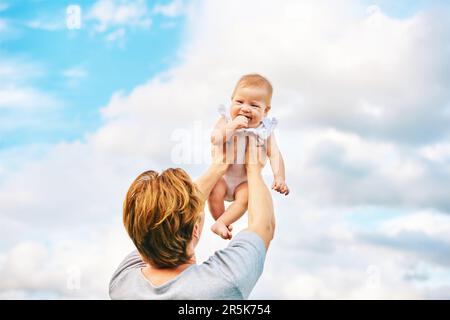 Glücklicher junger Vater, der draußen mit einem niedlichen Mädchen spielt, Familienleben, Dad hält das Kind hoch in der Luft Stockfoto