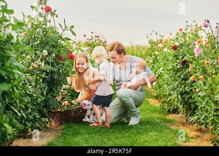 Glückliche junge Familie mit einem kleinen Mädchen und einem kleinen Jungen, die im wunderschönen Garten Blumen pflücken Stockfoto