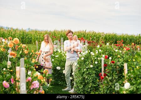 Glückliche junge Familie mit einem kleinen Mädchen und einem kleinen Jungen, die im wunderschönen Garten Blumen pflücken Stockfoto