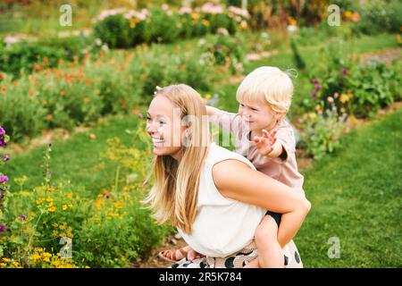 Außenporträt einer glücklichen jungen Mutter, die mit einem kleinen Sohn im Garten spielt, Familienleben Stockfoto