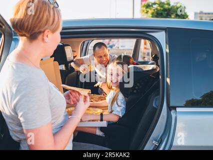 Ein positiv lächelndes Mädchen im Kindersitz, während der Familienausflug mit der Bremse aufgehört hat, gerade gekochte italienische Pizza zu essen. Glückliche Familienmomente, Kindheit, Fast Food Stockfoto