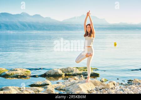 Wunderschöne gesunde Frau, die Yoga-Übungen draußen am wunderschönen Bergsee praktiziert Stockfoto