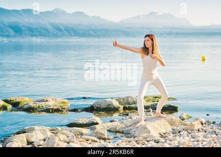 Wunderschöne gesunde Frau, die Yoga-Übungen draußen am wunderschönen Bergsee praktiziert Stockfoto