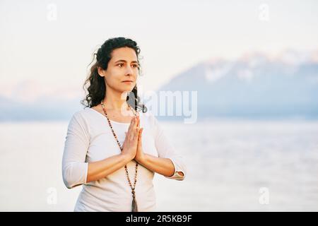 Wunderschöne spirituelle Frau, die am See meditiert, weiße Kleidung trägt Stockfoto