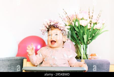 Frühlingsporträt eines niedlichen Babys, das in einem Stuhl sitzt und ein Blumenkopfband trägt Stockfoto