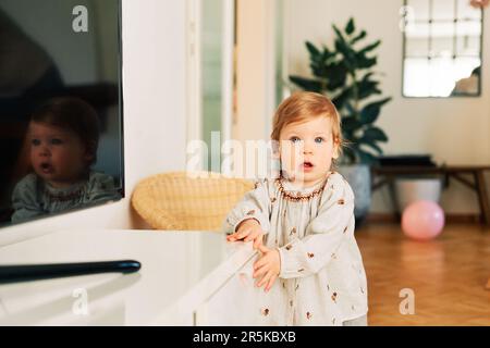 Innenporträt eines lustigen Kleinkindes, das versucht, die Schublade zu öffnen Stockfoto