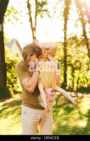 Familienzeit, Vater hält Sohn kopfüber, Eltern spielen mit Kind im Sommerpark, glückliche Kindheit Stockfoto