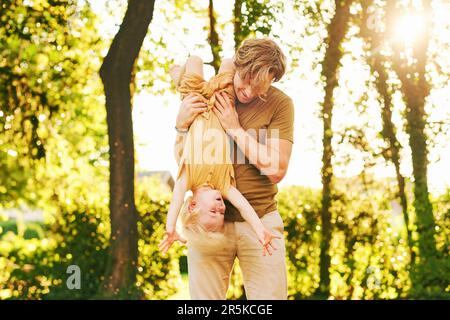 Familienzeit, Vater hält Sohn kopfüber, Eltern spielen mit Kind im Sommerpark, glückliche Kindheit Stockfoto