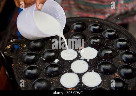 Gekürzte Hand, die Kokosnuss-Reis-Pfannkuchen in eine Pfanne gießt Stockfoto