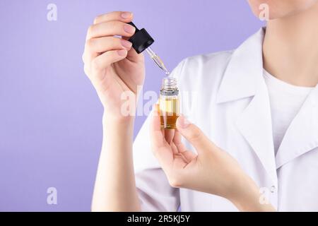 Eine Ärztin hält eine Flasche mit einer durchsichtigen gelben Flüssigkeit in den Händen. Alternative medizinische Cannabisbehandlung bei verschiedenen Krankheiten. Stockfoto