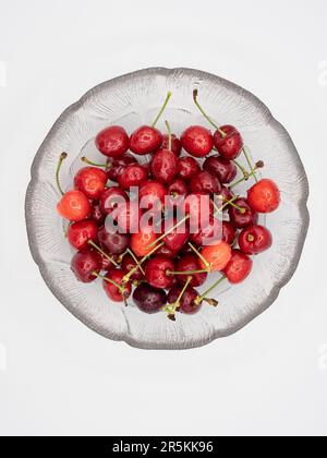 Rote Bio-Kirschen, glitzernd mit erfrischenden Wassertröpfchen, elegant präsentiert in einer unberührten Glasschüssel, perfekt isoliert auf einem sauberen weißen Bach Stockfoto