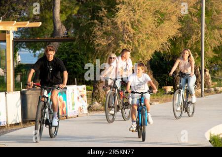 Vodice, Kroatien - 30. Mai 2023: Promenade mit Pinien am Meer und Fahrrad fahrenden Menschen Stockfoto