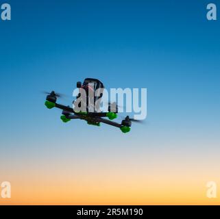 freestyle FPV-Drohne im Himmel bei Sonnenuntergang, im Flug, Rückansicht Stockfoto