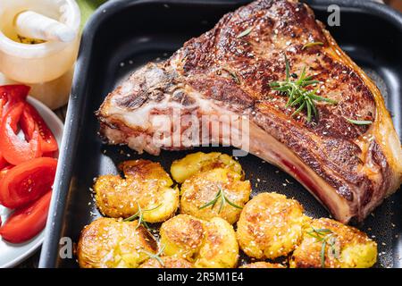 Erstklassiges Steak mit gebackenen Kartoffeln, serviert in einem Metalltablett. Gewürzt mit Rosmarin, Pfeffer und Knoblauch. Saftiges und köstliches Ribeye Steak Stockfoto