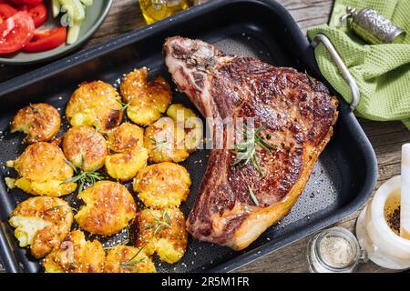 Erstklassiges Steak mit gebackenen Kartoffeln, serviert in einem Metalltablett. Gewürzt mit Rosmarin, Pfeffer und Knoblauch. Saftiges und köstliches Ribeye Steak Stockfoto