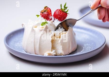 Zwei kleine pavlova-Minikuchen aus Baiser, dekoriert mit frischen Erdbeeren auf einem violetten Pastellteller. Helle Szene mit Blumen als Dekoration. Stockfoto