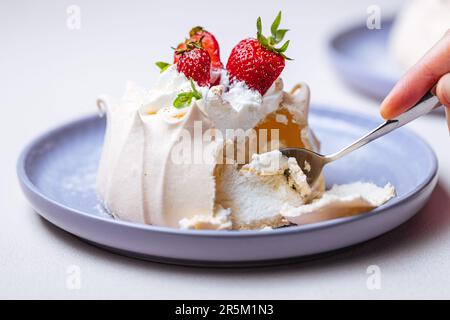 Zwei kleine pavlova-Minikuchen aus Baiser, dekoriert mit frischen Erdbeeren auf einem violetten Pastellteller. Helle Szene mit Blumen als Dekoration. Stockfoto