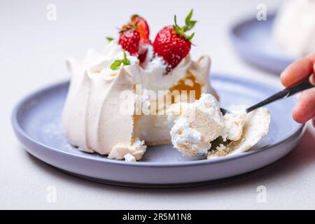 Zwei kleine pavlova-Minikuchen aus Baiser, dekoriert mit frischen Erdbeeren auf einem violetten Pastellteller. Helle Szene mit Blumen als Dekoration. Stockfoto